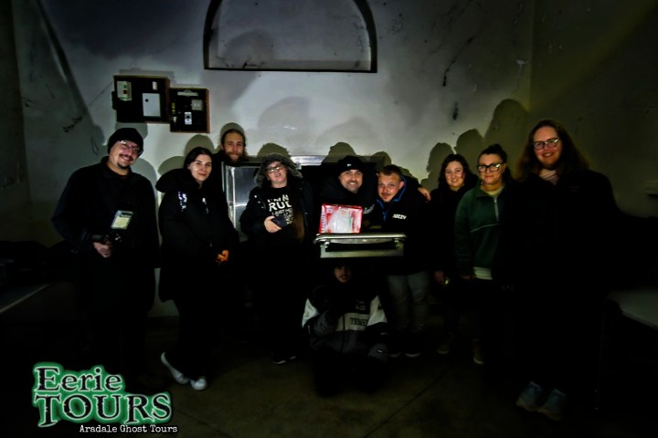 Group of people posing indoors with ghost hunting equipment.