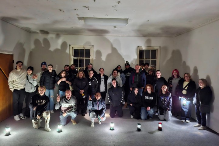 Group of people indoors posing with flashlights creating shadows on the wall.